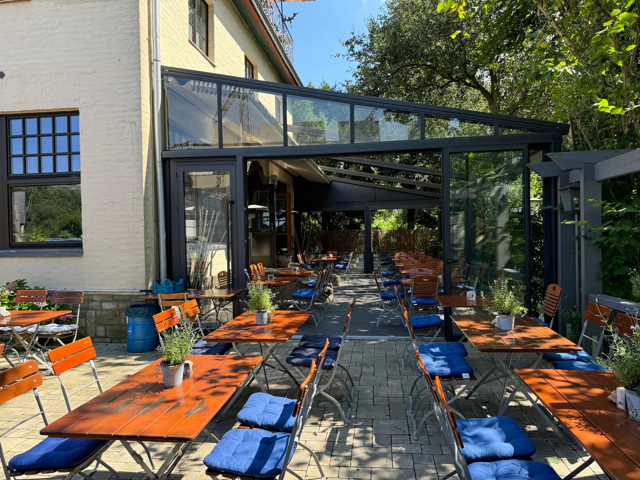 Menschenleerer Biergarten der Margaretenhöh mit Holztischen unter alten Bäumen