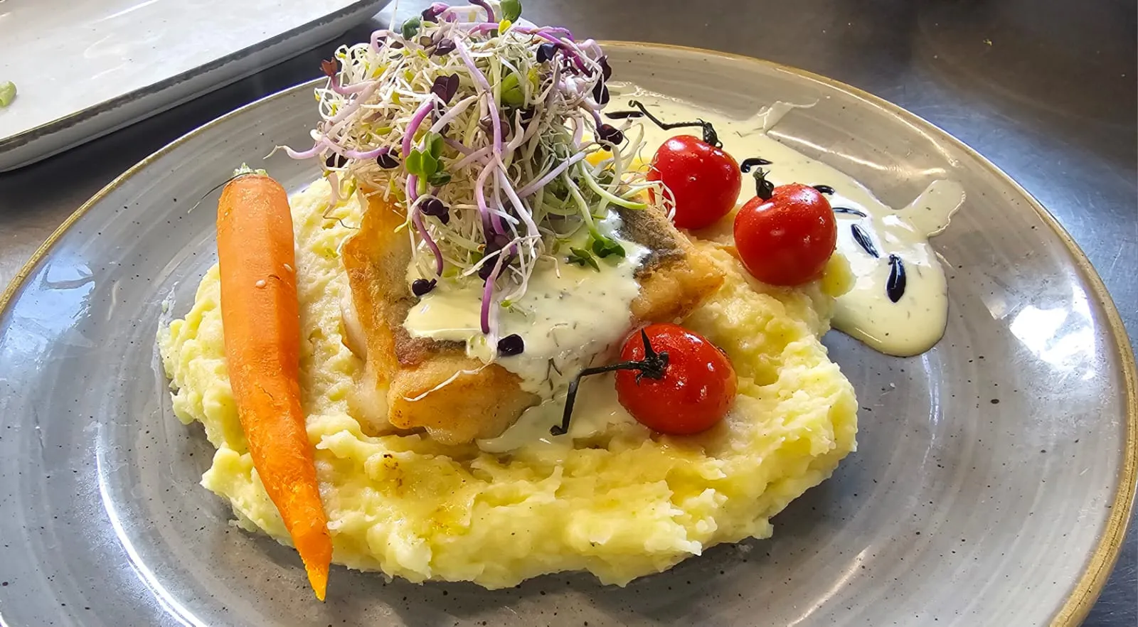 Angerichtetes Fischgericht auf Kartoffelpüree mit Möhren, Tomaten und Sprossen